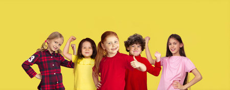 Strong. Portrait of little caucasian children gesturing isolated on yellow studio background with copyspace. Cheerful kid models. Concept of human emotions, facial expression, sales, ad, childhood.の写真素材