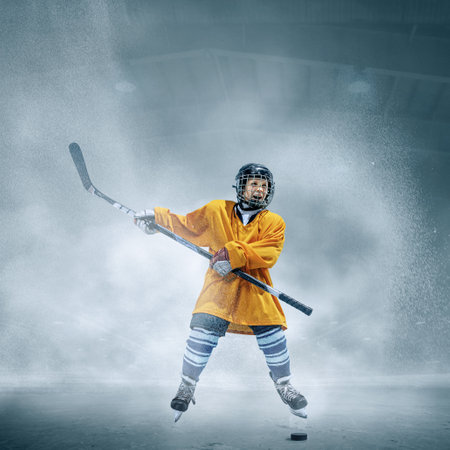 Winner. Little hockey player with the stick on ice court and smoke background. Sportsboy wearing equipment and helmet training in action. Concept of sport, childhood, motion, movement, action.の写真素材
