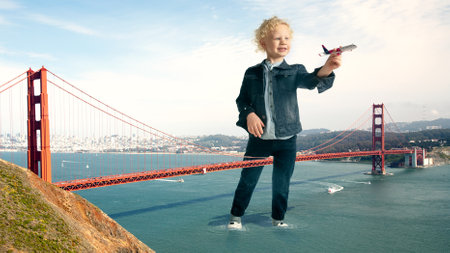 See the world by childrens eyes - little cute curly boy playing with big airplane standing on the bridge. Dreamworld in childhood. Happy caucasian little model. Life game with playground everywhere.の写真素材