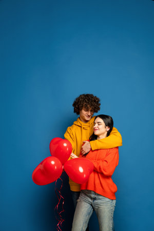 Heart balloon, embracing. Beautiful couple in love on blue studio background. Valentines Day, love, relationship and human emotions concept. Copyspace. Young man and woman look happy together. Flyerの写真素材