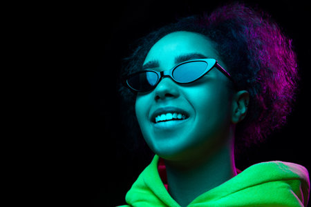 Eyewear. African-american womans portrait isolated on dark studio background in multicolored neon...