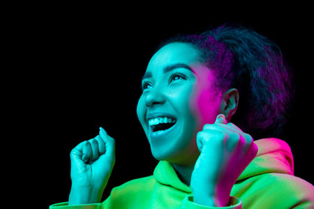 Excited. African-american womans portrait isolated on dark studio background in multicolored neon...