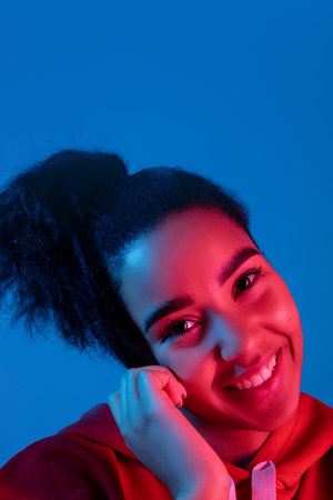 Happiness, cheerful. African-american womans portrait on blue studio background in red-pink neon light. Beautiful female model. Concept of human emotions, facial expression, sales, ad, fashion.の写真素材