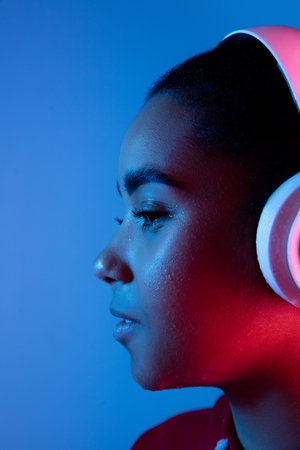 Attented. African-american womans portrait on blue background in red-pink neon light. Listening to...