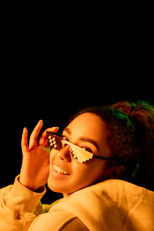 Style. African-american womans portrait isolated on dark background in mixed neon light. Wearing trendy pixel eyewear. Concept of human emotions, facial expression, sales, ad, fashion. Copyspace.の写真素材