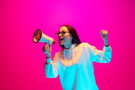 Shouting. Caucasian womans portrait isolated on pink studio background in mixed neon light. Wearing trendy eyeglasses. Concept of human emotions, facial expression, sales, ad, fashion. Copyspace.の写真素材