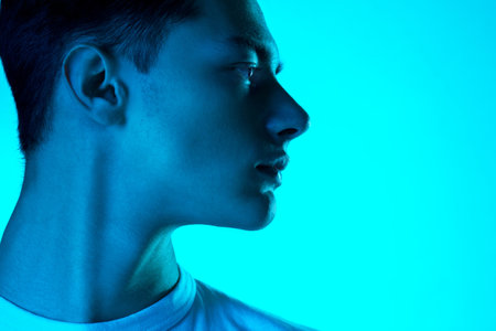 At side. Handsome caucasian mans portrait isolated on blue studio background in neon, monochrome....