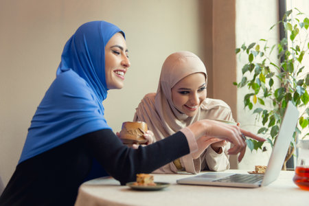 Laughting. Beautiful arab women meeting at cafe or restaurant, friends or business meeting. Spending time together, talking, laughting. Muslim lifestyle. Stylish and happy models with make up.の写真素材