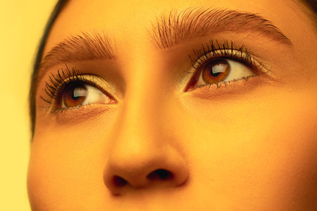 Eyes on. Beautiful east woman close up portrait in golden colored neon light, monochrome. Details,...