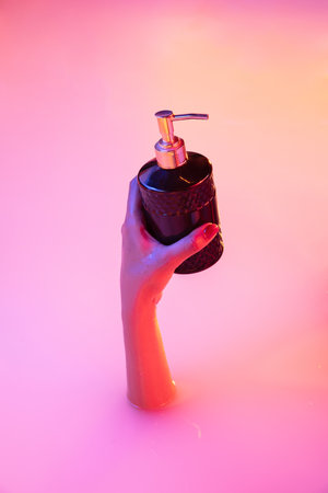 Close up female hand gesturing from the milk bath with soft white glowing in neon light. Copyspace for advertising. Holding sanitizer, soap bottle, covid prevention, healthcare. Modern neoned colors.の写真素材