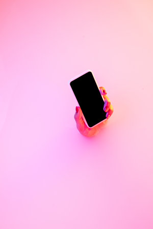 Tech. Close up female hand gesturing from the milk bath with soft white glowing in neon light. Copyspace for advertising. Holding cellphone with blank screen, device, gadget. Modern neoned colors.の写真素材