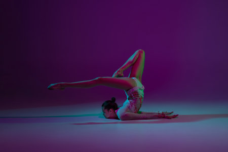 Balance. Young female athlete, rhythmic gymnastics artist dancing, training isolated on purple...