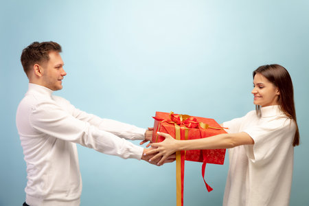 Surprise. Beautiful couple in love on blue studio background. Saint Valentines Day, love, relationship and human emotions concept. Copyspace. Young man and woman look happy together.の写真素材