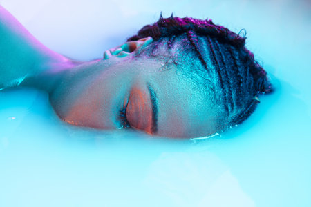 Sleep. Beautiful female face in the milk bath with soft glowing in blue-pink neon light. Copyspace...