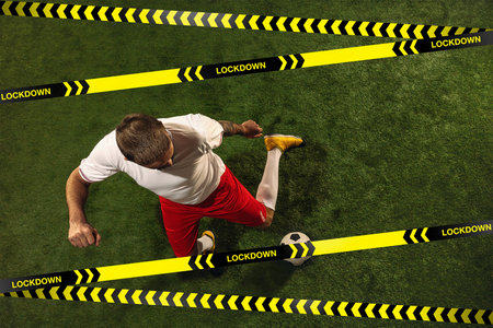 Football or soccer player on grass background behind limiting tapes with word Lockdown.