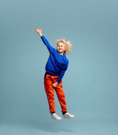 Flying. Happy curly boy isolated on blue studio background. Looks happy, cheerful. Copyspace for ad....