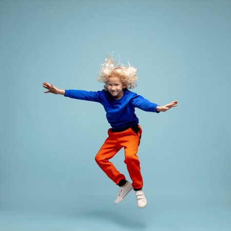 Air riding. Happy curly boy isolated on blue studio background. Looks happy, cheerful. Copyspace for ad. Childhood, education, emotions, facial expression concept. Jumping high, playing, having fun.の写真素材