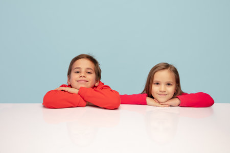 Sincere. Happy children isolated on blue studio background. Look happy, cheerful. Copyspace for ad. Childhood, education, emotions, facial expression concept. Sitting at the table dreamful, smilingの写真素材