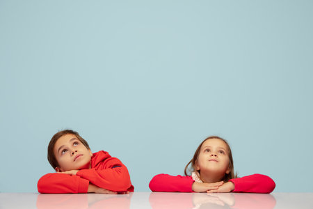 Looking up. Happy children isolated on blue studio background. Look happy, cheerful. Copyspace for ad. Childhood, education, emotions, facial expression concept. Sitting at the table dreamful, smilingの写真素材