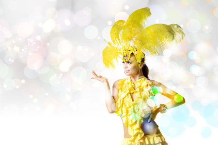 Beautiful young woman in carnival, stylish masquerade costume with feathers dancing on white studio...
