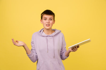 Shocked, asking with tablet. Caucasian girls portrait isolated on yellow background with copyspace. Beautiful female model in hoodie. Concept of human emotions, facial expression, sales, ad, fashion.の写真素材