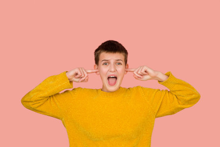 Closing ears. Caucasian girls portrait on coral pink studio background with copyspace for ad. Beautiful female model in sweater. Concept of human emotions, facial expression, sales, ad, fashion.の写真素材