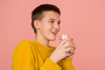 Joyful drinking water. Caucasian girls portrait on coral pink studio background with copyspace for ad. Beautiful model in sweater. Concept of human emotions, facial expression, sales, ad, fashion.の写真素材