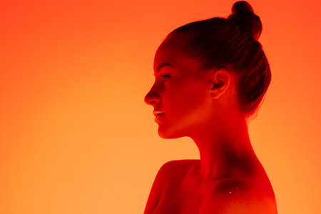Warm. Handsome womans portrait isolated on orange studio background in neon light, monochrome. Beautiful female model. Concept of human emotions, facial expression, sales, ad, fashion and beauty.の写真素材