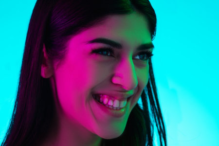 Cheerful. Close up brunette womans portrait isolated on blue studio background in mixed neon light. Beautiful female model. Concept of human emotions, facial expression, sales, ad, fashion.の写真素材