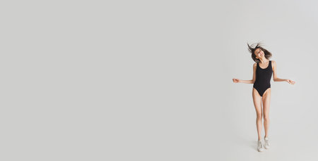 Dancing cheerful. Beautiful young womans isolated on white studio background. Having fun, happy, full length. Dancing, getting crazy mood, stylish posing. Fit girl in black sportive swimsuit. Flyer.の写真素材