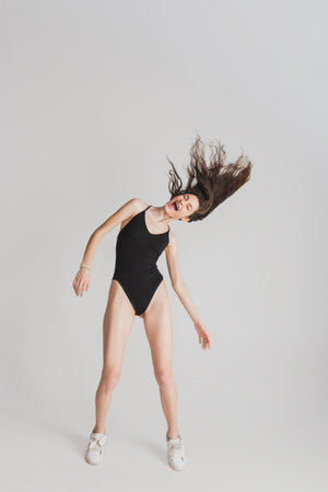Hair blowing. Beautiful young womans isolated on white studio background. Having fun, happy, full length. Dancing, getting crazy mood, stylish posing. Fit girl in black sportive swimsuit. Copyspace.の写真素材