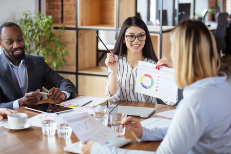 Graphs. Diverse group of co-workers having casual discussion in office. Executives during friendly discussion, month reporting, creative meeting. Concept of business, finance, occupation, job.の写真素材