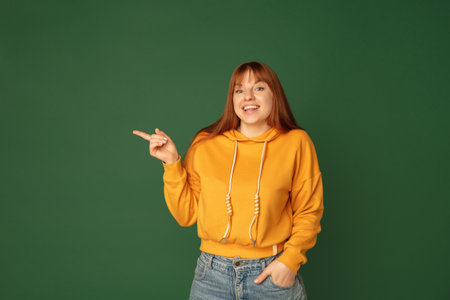 Pointing. Caucasian womans portrait isolated on green studio background with copyspace. Beautiful...