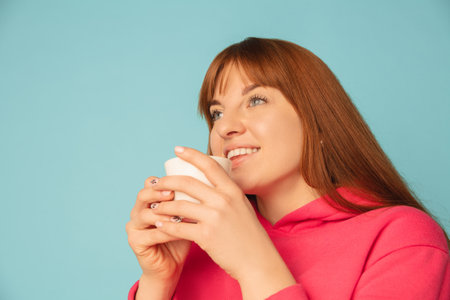 Enjoying coffee, tea. Caucasian womans portrait on blue studio background with copyspace. Beautiful...