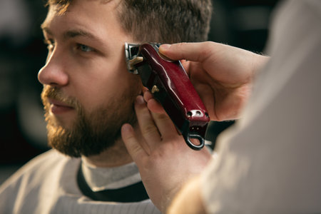 Delighted. Close up of client of master barber, stylist during getting care and new look of hairstyle. Professional occupation, male beauty and self-care concept. Soft colors and focus, vintage.の写真素材