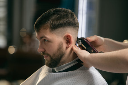 Fresh style. Close up of client of master barber, stylist during getting care and new look of hairstyle. Professional occupation, male beauty and self-care concept. Soft colors and focus, vintage.の写真素材