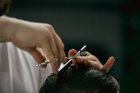 Close up hands of master barber, stylist with sccissors does the hairstyle to guy, young man. Professional occupation, male beauty concept. Cares of hair of client. Soft colors and focus, vintage.の写真素材