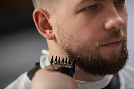 Close up of client of master barber, stylist during getting care and new look of mustache and beard. Professional occupation, male beauty and self-care concept. Soft colors and focus, vintage.の写真素材
