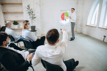 Stats. Male speaker giving presentation in hall at university workshop. Audience or conference hall. Rear view of unrecognized participants in face masks. Scientific, business event, training.の写真素材