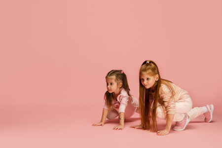Excitement. Happy kids, girls isolated on coral pink studio background. Look happy, cheerful. Copyspace for ad. Childhood, education, emotions, facial expression concept. Ready to run, having funの写真素材