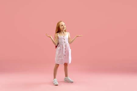 Astonished. Childhood and dream about big and famous future. Pretty longhair girl on coral pink studio background. Childhood, dreams, imagination, education, facial expression, emotions concept.の写真素材