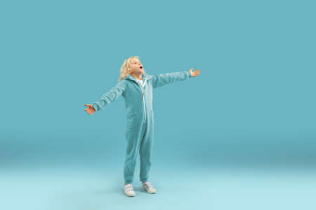 Greeting, shocked. Childhood and dream about big and famous future. Pretty curly boy isolated on blue studio background. Childhood, dreams, imagination, education, facial expression, emotions concept.の写真素材