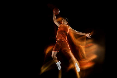 Fire. Young arabian muscular basketball player in action, motion isolated on black background in mixed light. Concept of sport, movement, energy and dynamic, healthy lifestyle. Training, practicing.の写真素材