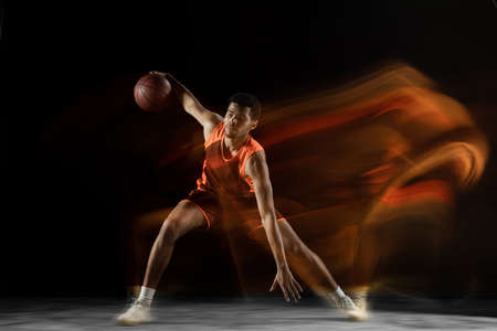Ready. Young arabian muscular basketball player in action, motion isolated on black background in mixed light. Concept of sport, movement, energy and dynamic, healthy lifestyle. Training, practicing.の写真素材