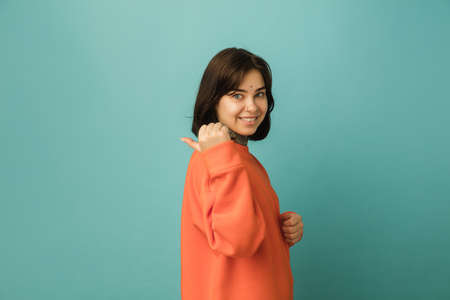 Pointing at side. Caucasian womans portrait isolated on blue background with copyspace. Beautiful...