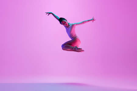 Flying, jumping. Young and graceful ballet dancer on pink studio background in neon light. Art, motion, action, flexibility, inspiration concept. Flexible caucasian ballet dancer, moves in glow.の写真素材