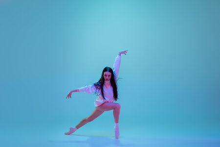 Strong. Young and graceful ballet dancer isolated on blue studio background in neon light. Art, motion, action, flexibility, inspiration concept. Flexible caucasian ballet dancer, moves in glow.の写真素材