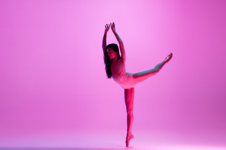 Flying, freedom. Young and graceful ballet dancer on pink studio background in neon light. Art, motion, action, flexibility, inspiration concept. Flexible caucasian ballet dancer, moves in glow.の写真素材