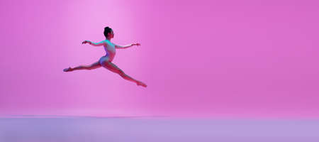Young and graceful ballet dancer isolated on pink studio background in neon light. Art, motion,...