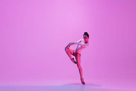 Urban style. Young and graceful ballet dancer on pink studio background in neon light. Art, motion, action, flexibility, inspiration concept. Flexible caucasian ballet dancer, moves in glow.の写真素材